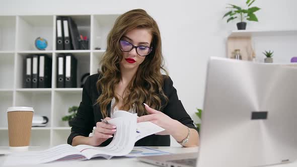 Business Lady in Eyeglasses in Stylish Wear and with Bright Make-up Working with Financial Papers