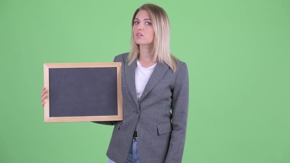 Stressed Young Blonde Businesswoman Holding Blackboard and Giving Thumbs Down