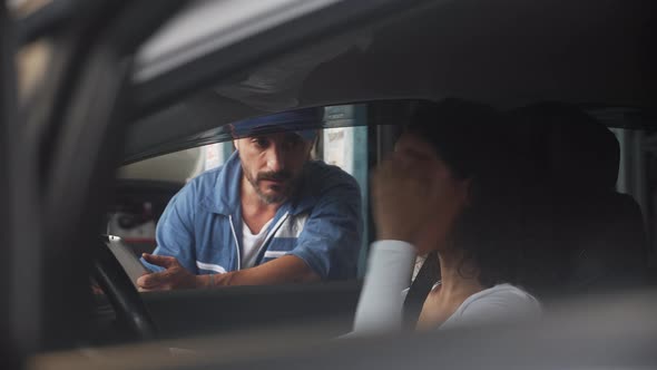 Young mechanic holding tablet talking and explaining with customer in car about problem engine.