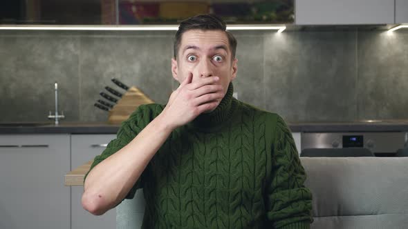 Shocked Man in Green Sweater Sits on Sofa at Home