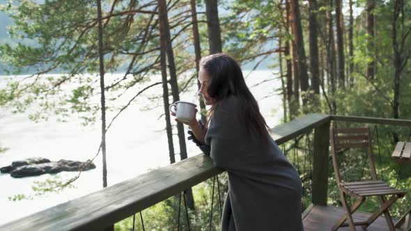 Beautiful Girl Wrapped in a Plaid on a Balcony in a Mountain House Enjoying a Cup of Tea. Attractive