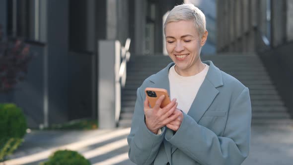 Happy Middle Aged Caucasian Woman Using Smartphone While Walking Near Business Centre