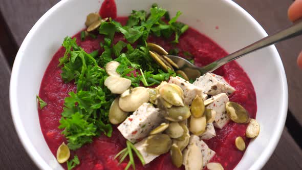 Close Up of Spoon Stirring Beet Soup Topped with Seeds and leaves.Healthy Life Concept.