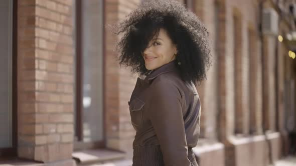 Rear View of Young African American Woman Walking Down Street Turning Around and Smiling