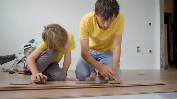 Father and His Little Son Install Laminate on the Floor in Their Apartment