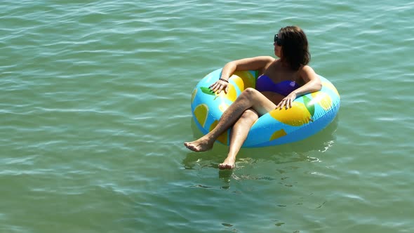 A sexy girl floats on an inflatable mattress on a beautiful white beach with clear water.