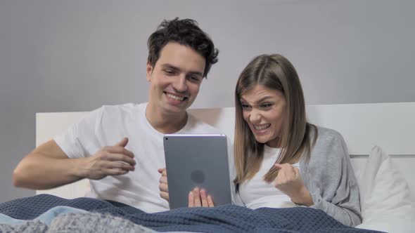 Young Couple Cheering for Win While Using Tablet in Bed