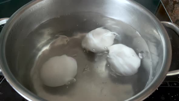 Chicken eggs cooking in a stainless steel pan with hot water boiling and the eggs are covered with m