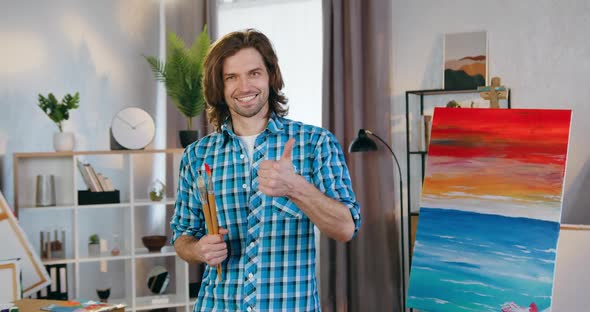Male Artist which Posing on Camera in Home Studio and Gesturing thumb Up