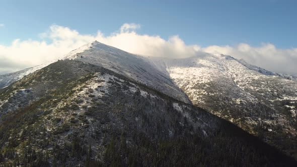 High mountain peaks covered with autumn spruce forest and high snowy summits.