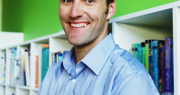 Portrait of smiling teacher holding a stack of books in library at school