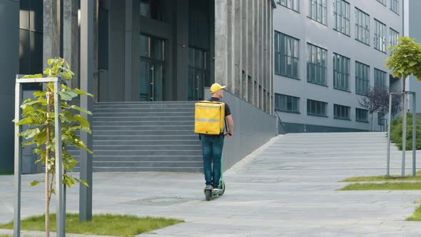 Delivery Man with Yellow Backpack Rides a Electric Scooter Through the City with