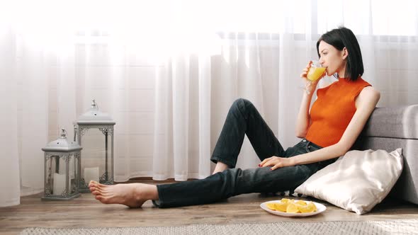 Young Woman Sitting on the Flor with Orange Juice