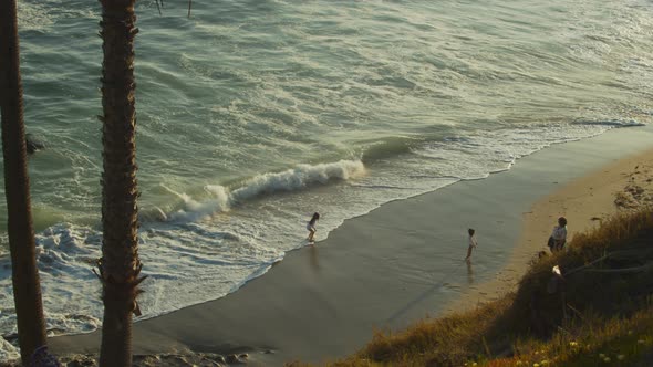 Young children at a Southern California beach during sunset joyfully play in the gentle ocean waves