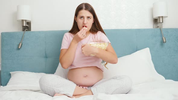 Concentrated Pregnant Woman Watching Movie on TV and Eating Popcorn From Big Bowl
