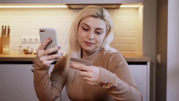 Beautiful attractive woman uses smartphone to shop on the Internet with a credit card from home