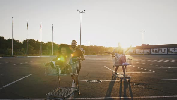 Young Multiracial Friends are Laughing and Racing on Shopping Carts at Deserted Parking Lot of