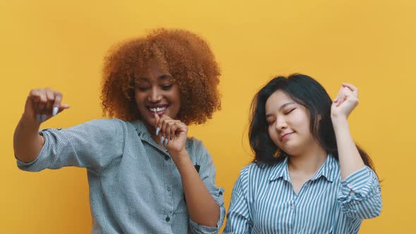 Two Young Happy Women Dancing. Isolated on Yellow Background