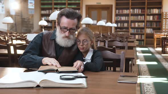 Old Bearded Grandfather in Glasses and Nice Granddaughter which Sitting in the Library