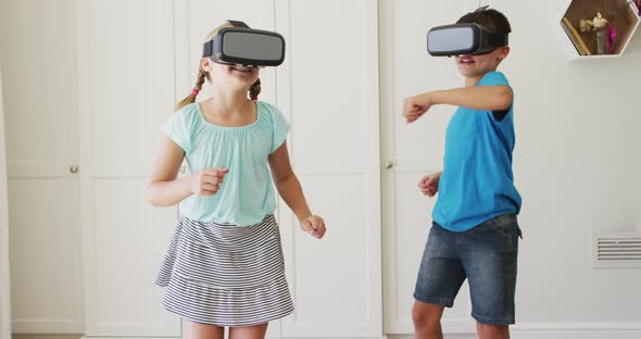 Caucasian brother and sister gesturing while wearing vr headset at home