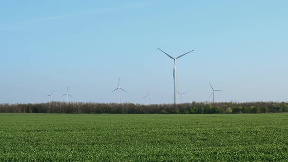 Aerial fly around wind turbines across spring agricultural field.