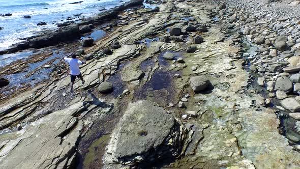 Tracking shot of a young man running on a rocky ocean beach shoreline