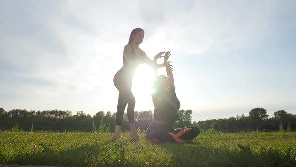 Cheerful Trainer and Positive Woman Beaming While Doing a Stretching Exercise Outdoors at Sunset