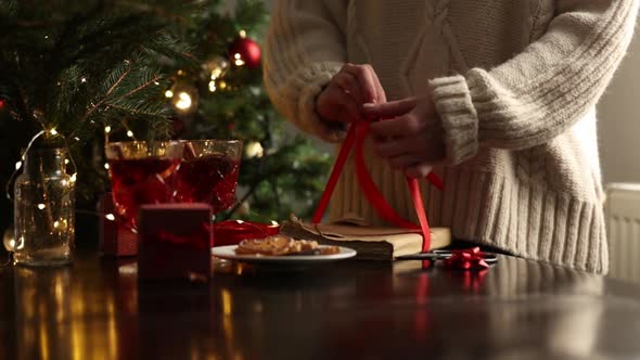 Woman in sweater is wrapping a Christmas gift on a table