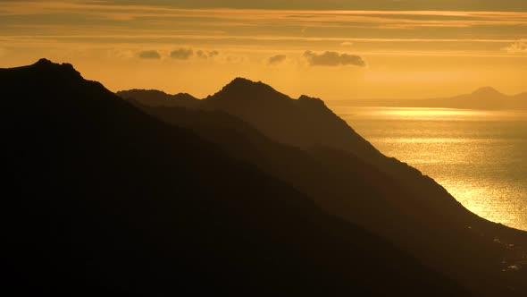 Aerial cinematic shot of majestic mountain silhouettes backed by brilliant refection of the sun on t