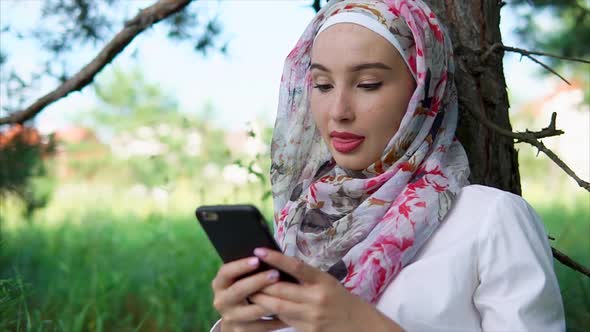 A Woman with a Hijab Chatting with Friends on a Smartphone a Lady Is in the Park