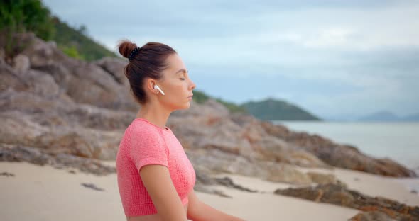 Woman on Yoga Mat on the Beach She is in Lotus Pose Listening the Music and Meditating