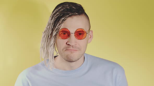 Young Handsome Man with Dreadlocks in Bright Sunglasses Looking at Camera Showing Tongue on Yellow