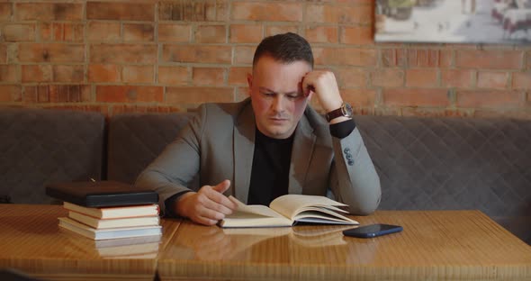 A Man With A Serious Expression Reads A Book And At This Time Someone Is Calling On A Mobile Phone