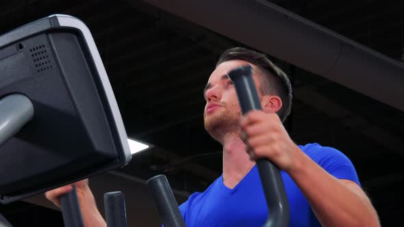 A Young Fit Man Trains on an Elliptical Trainer in a Gym - Closeup From Below