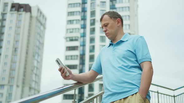 Portrait of a Young Man with a Mobile Phone in His Hands Stands on the Stairs Buildings Background