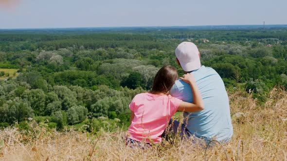 Beautiful Summer Landscape. Man and Little Girl, Dad and Daughter, Sit on Cliff Edge, Admiring