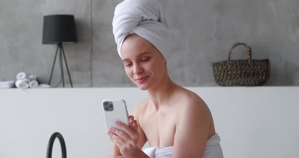 Closeup Portrait of Half Naked Beautiful Woman Wrapped in Bath Towel Using a Mobile Phone Texting