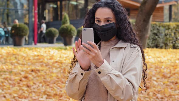 Beautiful Girl in Medical Mask Stand in Autumn Park Hispanic Young Woman Making Video Call Outdoors