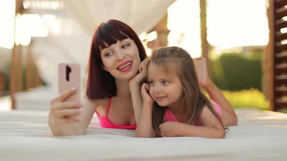 Relaxed Young Woman and Her Daughter Watching Movie or Having Video Chat on Smartphone