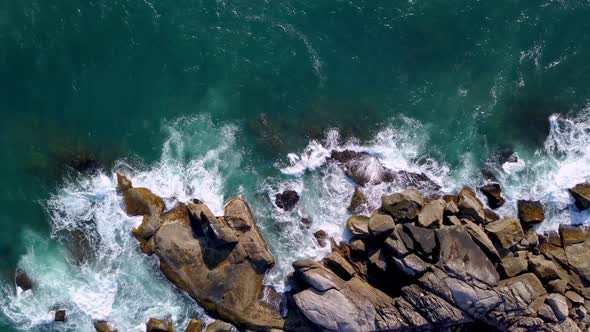 Aerial top down shot of waves breaking on the boulders in Trilha da Sepultura, Bombinhas. Jib down