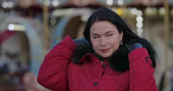 Close-up of Middle-aged Brunette Caucasian Woman in Red Coat Putting on Hood. Beautiful Positive