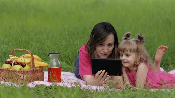 Family Weekend Picnic. Daughter Child Girl with Mother Study Lessons on Tablet. Distance Education