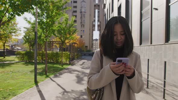 Young Adult Asian Woman Working on Her Smart Phone While Walking in the City