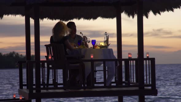 A man and woman couple eat dinner and dine in a hut on a tropical island beach