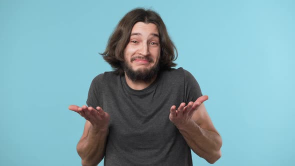 Portrait of Innocent Guy with Beard and Brown Hair Shrugging and Gesturing with Both Hands Meaning