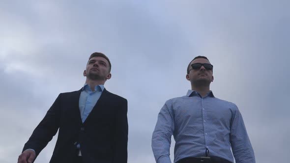 Two Young Businessmen Walking in the City with Blue Sky at Background. Handsome Coworkers Commuting