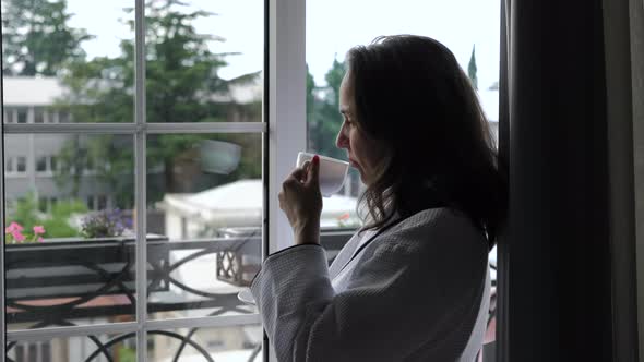 Female in Bathrobe Drinking Coffee By the Window