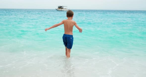 Young boy entering turquoise sea water, summer holidays.