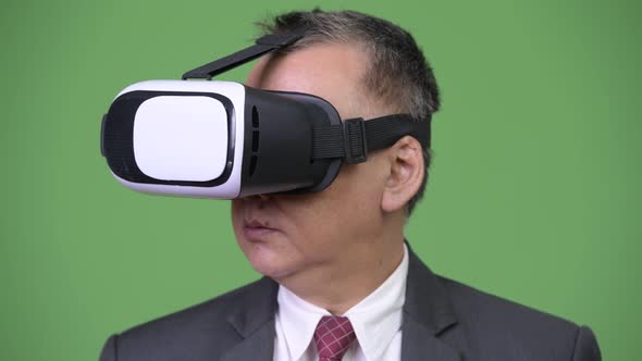 Mature Japanese Businessman Using Virtual Reality Headset Against Green Background