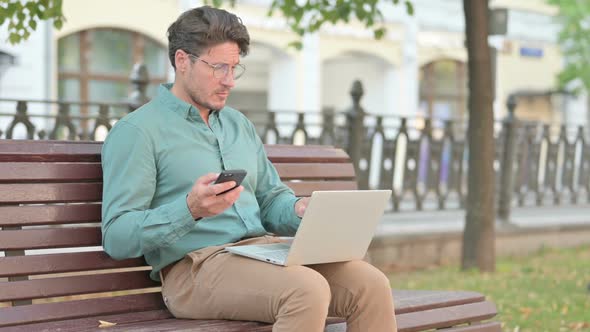 Man Browsing on Smartphone while working on Laptop
